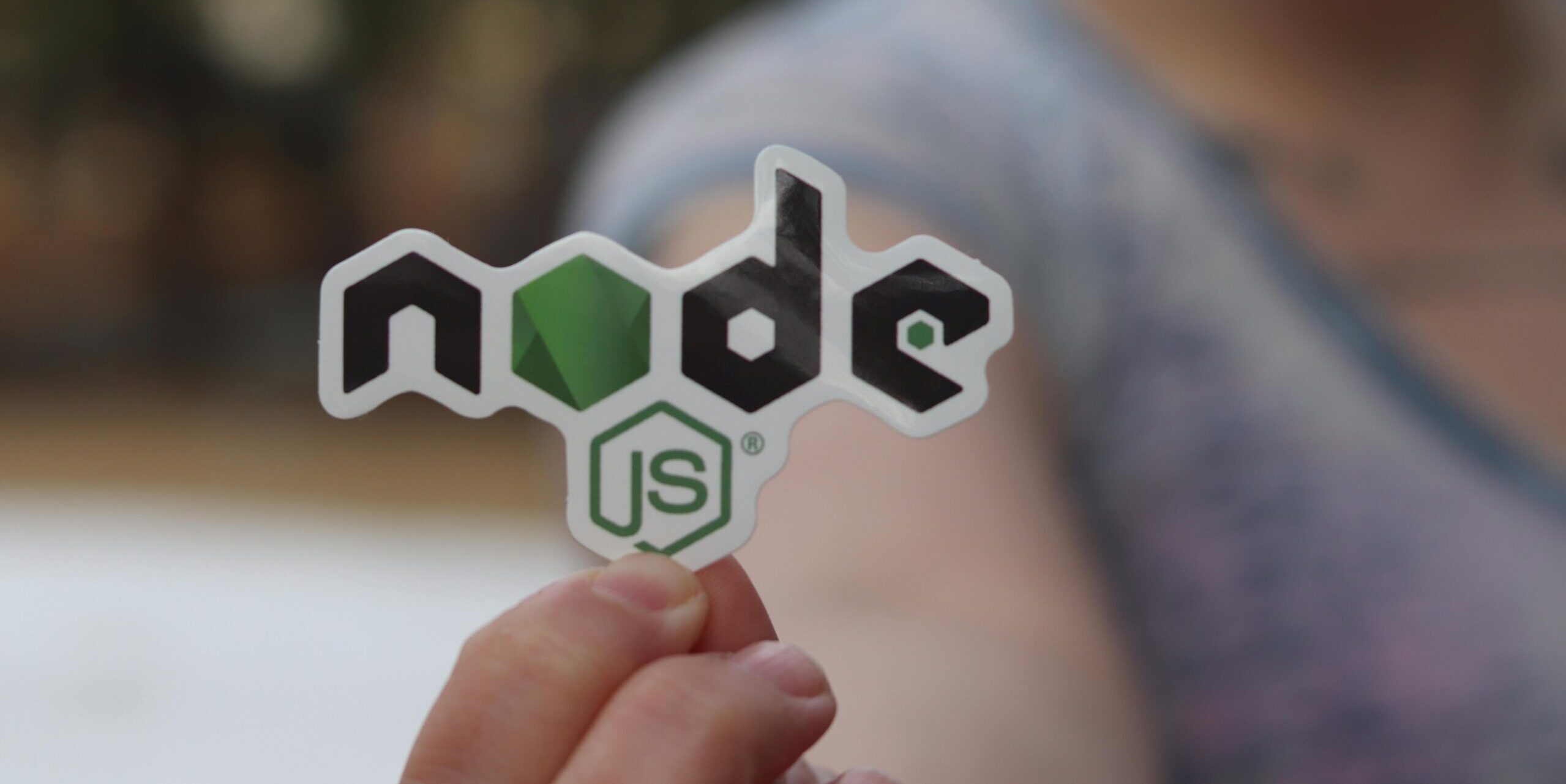 A person holding a Node.js sticker with a blurred background, close-up shot.
